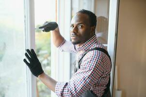 bonito jovem africano americano homem instalando baía janela dentro Novo casa construção local foto