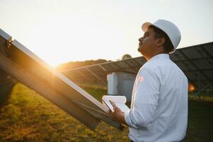 retrato do jovem indiano masculino engenheiro em pé perto solar painéis, com Claro azul céu fundo, renovável e limpar \ limpo energia. habilidade Índia, cópia de espaço foto