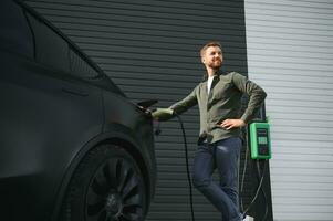 uma homem carrinhos perto uma cobrando estação e cobranças dele elétrico carro foto