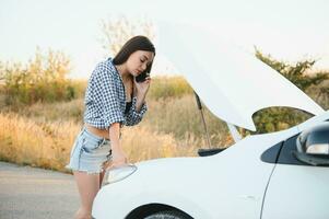 a jovem menina quebrou a carro e ela aberto a de capuz e tentou para reparar a carro em a estrada. uma mulher chamadas em uma Smartphone com uma carro evacuação serviço foto