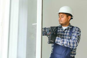 indiano serviço homem instalando janela com Chave de fenda foto