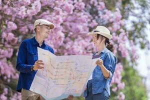 ásia casal turista segurando cidade mapa enquanto caminhando dentro a parque às cereja Flor árvore durante Primavera sakura flor festival foto