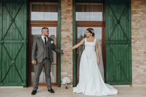 a noiva e noivo estão em pé contra a fundo do verde janelas. à moda noiva e noivo. Casamento foto. fácil atmosfera foto