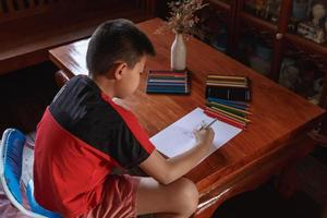 um menino sentado em sua casa desenhando e pintando. foto