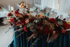 a Casamento mesa do a noiva e noivo, decorado com vermelho flores, azul veludo, é fez dentro vermelho e azul. flores em fica. Casamento detalhes. luz foto