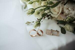 Rosa e branco flores e dois ouro Casamento argolas e abotoaduras em uma branco fundo. Casamento acessórios foto