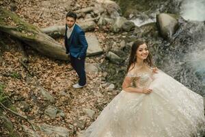 Casamento casal perto uma montanha rio. ela é dentro a primeiro plano dentro foco. noivo e noiva. Casamento foto sessão dentro natureza. foto sessão dentro a floresta do a noiva e noivo.