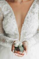 a noiva dentro uma lindo vestir é em pé de a janela com a do noivo flor dentro dele mãos. casamento. Casamento ramalhete manhã do a noiva. uma feliz noiva é esperando para a noivo. foto