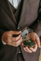 Casamento ouro argolas em uma decorativo vidro caixa com de madeira verde musgo, em pé dentro a mãos do a noivo, fechar-se. joalheria conceito foto