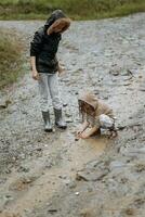 dois feliz pequeno meninas do europeu aparência jogando dentro poças durante chuva dentro verão. crianças estão jogando dentro a chuva. criança jogando dentro natureza ao ar livre. a menina goza a chuva. foto