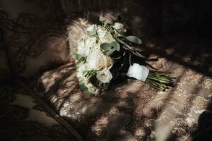 acessórios para a do noivo casamento. uma ramalhete do branco rosas e vegetação carrinhos em a costas do a sofá perto a janela. lindo flores luz e sombras foto