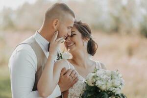 Casamento foto dentro natureza. a noiva e noivo estão em pé dentro a floresta, a noivo abraços dele Amado a partir de atrás e Beijos dela, ela sorrisos sinceramente. retrato. verão Casamento