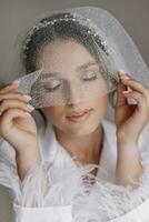 manhã do noiva antes a casamento. lindo jovem mulher com grandes véu dentro uma branco manto. natural beleza e profissional maquiagem.menina dentro branco renda boudoir vestir. foto