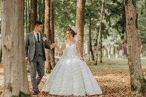 a noiva e noivo andar mão dentro mão através a floresta. feliz casal. Casamento foto. casal dentro amar. alta árvores, ângulo amplo foto. perfeito luz foto