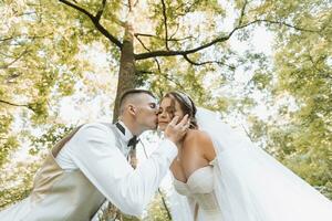 retrato do uma lindo casal dentro amor em seu Casamento dia. uma andar dentro a parque dentro a luz solar. surpreendente Beijos e abraços do a noiva e noivo com uma ramalhete foto