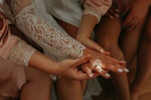 a damas de honra admirar a Casamento anel em a da noiva dedo. a noiva e dela Diversão amigos estão a comemorar uma solteira Festa. noiva e amigos dentro a quarto foto