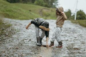 dois feliz pequeno meninas do europeu aparência jogando dentro poças durante chuva dentro verão. crianças estão jogando dentro a chuva. criança jogando dentro natureza ao ar livre. a menina goza a chuva. foto