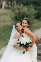 Casamento foto dentro natureza. uma morena noiva dentro uma branco grandes vestir e dela amigo dentro uma nu vestir estão abraçando e sorridente e posando. jovem mulheres. emoções