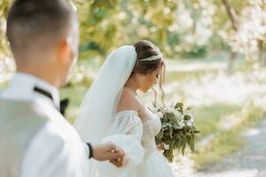 retrato do uma lindo casal dentro amor em seu Casamento dia. uma andar dentro a parque dentro a luz solar, a noiva conduz a noivo. surpreendente Beijos e abraços do a noiva e noivo com uma ramalhete foto