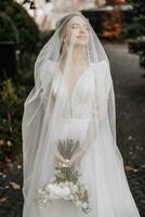 uma lindo noiva com dela olhos fechadas é em pé segurando dela ramalhete. retrato do uma jovem lindo noiva. casamento. retrato com uma véu sobre dela face foto