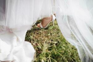 mulheres pernas dentro Casamento sapato, em a fundo do verde Relva e uma Casamento vestir. detalhes. Casamento acessórios. Primavera casamento. foto