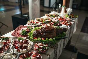 bufê mesa às a casamento. a sortimento do lanches em branco pratos em pé em uma estilo ucraniano toalha de mesa. banquete serviço. comida, lanches com queijo, presunto, prosciutto e verdes. foto