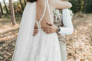 Casamento foto dentro natureza. a noiva abraços a noivo. do noivo mãos em a da noiva cintura. vezes lindo ombros do a noiva. detalhes