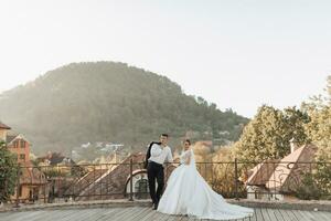 Casamento retrato. a noivo dentro uma Preto terno e a Loiras noiva estão de pé, abraçando, posando segurando uma ramalhete debaixo uma árvore. foto sessão dentro natureza. lindo cabelo e Maquiagem