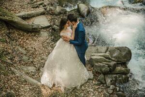 Casamento casal é abraçando perto a montanha rio. noivo e noiva . natureza Casamento sessão de fotos. foto sessão dentro a floresta do a noiva e noivo.