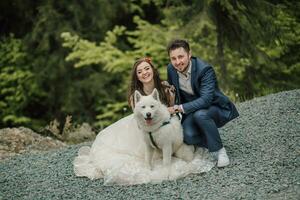 noiva com grandes cabelo, sorridente sinceramente, feliz à moda noivo, foto com cachorro. Casamento foto sessão dentro natureza. foto sessão dentro a floresta do a noiva e noivo.