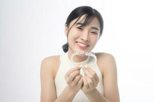 jovem mulher sorridente segurando aparelho invisalign sobre estúdio de fundo branco, saúde bucal e conceito ortodôntico. foto