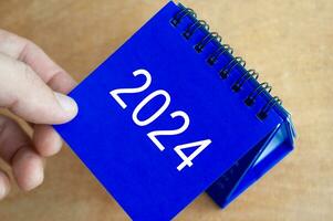 mão mostrando ano 2024 mesa calendário em de madeira fundo. calendário Novo ano conceito. foto