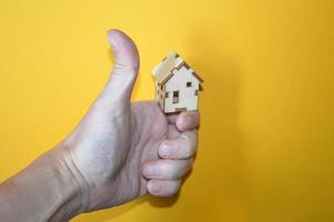 pequena casa de madeira na mão de um homem em um fundo amarelo foto