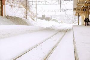 lado de fora Visão do local trem estação e metal grandes Ferrovia rastrear coberto de Grosso neve dentro inverno estação com pessoas esperando trem às trem plataforma em branco nebuloso fundo do trem estação. foto