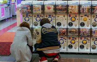 osaka, Japão, janeiro 14 2019 - Adolescência meninas jogando gachapong vending máquina dentro Japão brinquedos fazer compras. gachapong é 1 do vending máquina dispensada cápsula brinquedos, popular entre turistas visitando Japão. foto