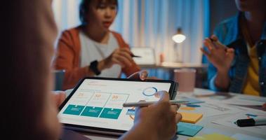 close-up asiáticos empresários reunindo plano de análise estatísticas brainstorm e cabeçalho da equipe seguram tablet gráfico gráfico ponto e funcionário tomam nota na noite do escritório em casa. conceito de sucesso de estratégia de finanças.