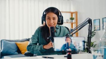 O influenciador adolescente da Ásia usa o conteúdo de gravação de fone de ouvido com microfone e telefone inteligente para que o público on-line ouça em casa. estudante feminino podcaster fazer podcast de áudio de seu estúdio em casa. foto