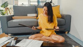 mulher jovem asiática feliz desempacotando a caixa e lendo as instruções para montar a mobília nova decorar a mesa de construção de casa com caixa de papelão na sala de estar em casa. foto