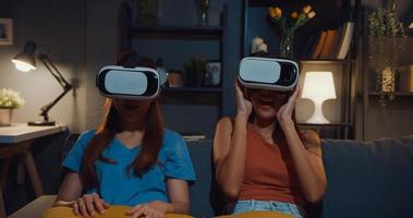 mulheres asiáticas atraentes desfrutam da experiência de compra on-line do momento feliz com o site de fone de ouvido de óculos de realidade virtual na sala de estar do sofá em casa à noite escura. usando com fone de ouvido de óculos de vr para a hora do filme. foto