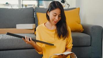 mulher jovem asiática feliz desempacotando a caixa e lendo as instruções para montar a mobília nova decorar a mesa de construção de casa com caixa de papelão na sala de estar em casa. foto