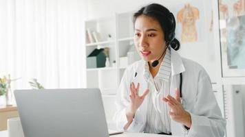 jovem doutora da Ásia em uniforme médico branco com estetoscópio, usando o computador laptop, falando por videoconferência com o paciente na mesa na clínica de saúde ou hospital. consultoria e conceito de terapia. foto