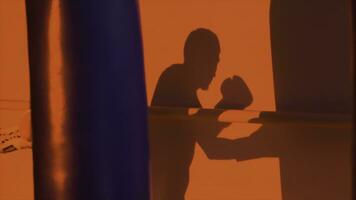 silhueta ou sombra do uma boxer soco uma soco saco fechar acima, vermelho luz fundo. silhueta do jovem masculino boxer batendo soco saco em vermelho fundo. homem atleta em pé e boxe. foto
