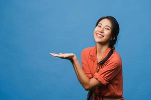 retrato de uma jovem asiática sorrindo com uma expressão alegre, mostra algo incrível no espaço em branco em um pano casual e olhando para a câmera isolada sobre fundo azul. conceito de expressão facial. foto
