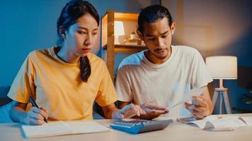 O homem e a mulher do casal asiático de estresse usam a calculadora para calcular o orçamento familiar, dívidas, despesas durante a crise econômica financeira em casa à noite. problemas de dinheiro do casamento, conceito de plano de orçamento familiar. foto