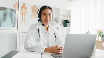 jovem doutora da Ásia em uniforme médico branco com estetoscópio, usando o computador laptop, falando por videoconferência com o paciente na mesa na clínica de saúde ou hospital. consultoria e conceito de terapia. foto