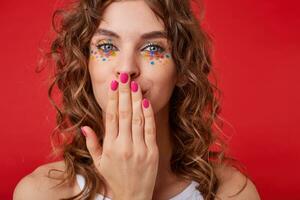 bonita jovem senhora com cachos parece às a Câmera, Beijos dela mão com Rosa manicure, parece positivo, carrinhos sobre a vermelho fundo foto