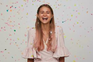 estúdio tiro do adorável feliz jovem grandes cabelos senhora rindo alegremente enquanto tendo aniversário festa com dela amigos, em pé sobre branco fundo dentro multicolorido confete foto