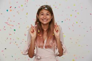 feliz jovem alegre senhora com luz Castanho grandes cabelo cruzando dedos para Boa sorte enquanto fazer desejo em dela aniversário, tendo Diversão com dela amigos em festa, posando sobre branco fundo foto