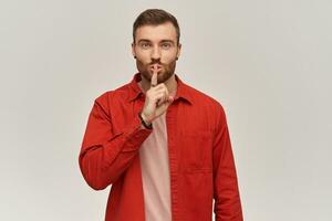 feliz atraente jovem barbudo homem dentro vermelho camisa mostrando silêncio gesto e olhando às Câmera sobre branco fundo foto