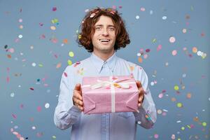 uma homem veio para uma feriado, dando uma presente, dentro dele mãos uma Rosa caixa amarrado com uma branco fita, sorridente e pronto para dizer muitos caloroso palavras para uma aniversário cara. foto